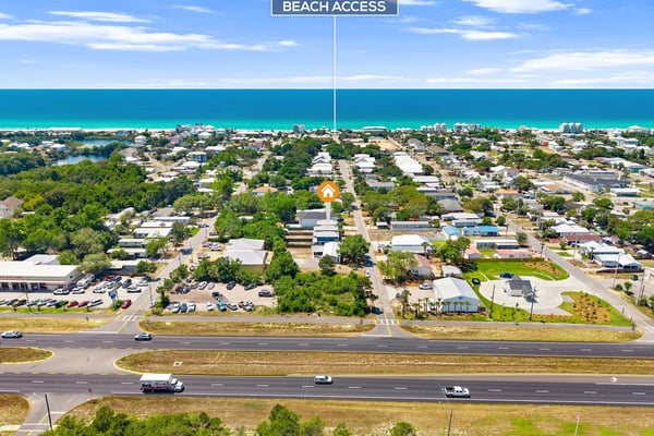 Aerial view of coastal residential neighborhood with turquoise ocean, marked beach access point, and highway below