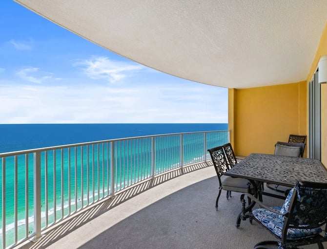 Beachfront balcony with metal dining table, chairs, and retractable awning overlooking turquoise ocean and sandy beach